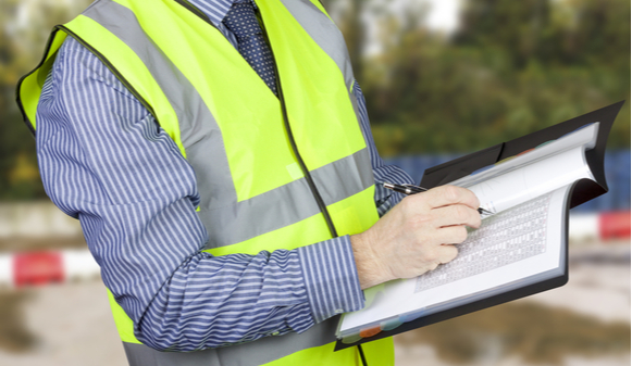 Building surveyor in hi vis checking data on building site